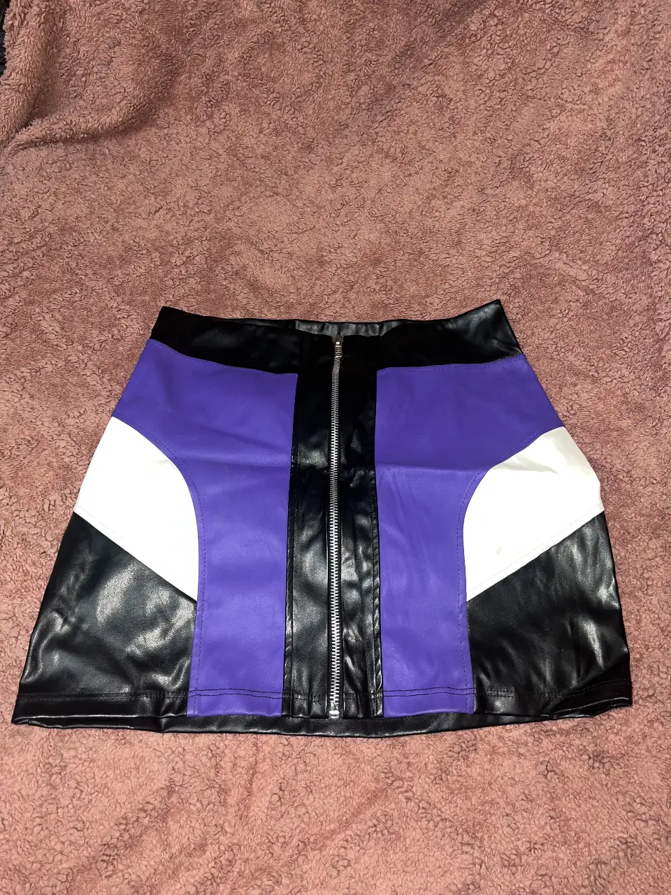Pollera de cuero sintético con diseño en bloques de color. Posee cierre frontal y detalles en negro, blanco y violeta. Ideal para un look moderno y audaz.