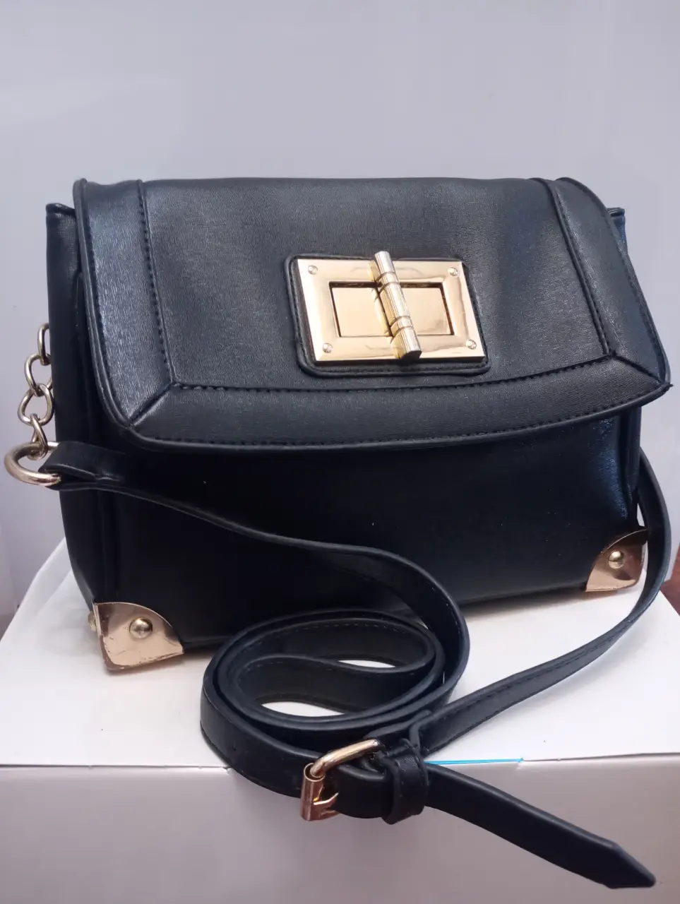 Cartera bandolera negra con detalles dorados. Diseño elegante con cierre de hebilla y correa ajustable. Ideal para un look sofisticado.