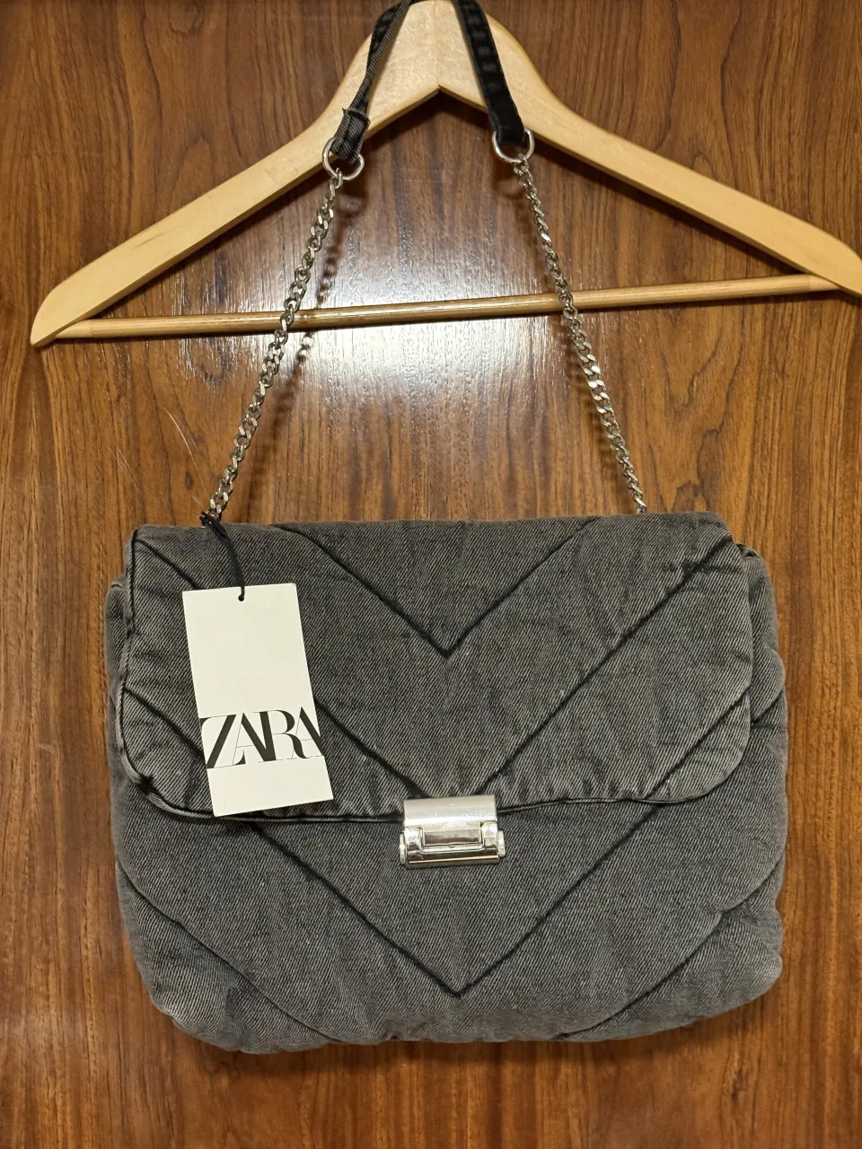 Bolso acolchado de jean gris con diseño de rombos y cierre metálico. Posee correa de cadena y tira de jean.