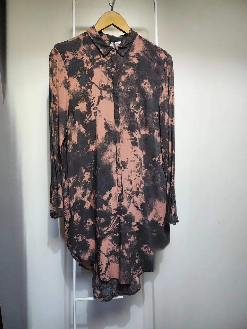 Camisa larga con estampa tie-dye en tonos rosas y negros. Posee cuello camisero y botones al frente. Ideal para un look casual y descontracturado.