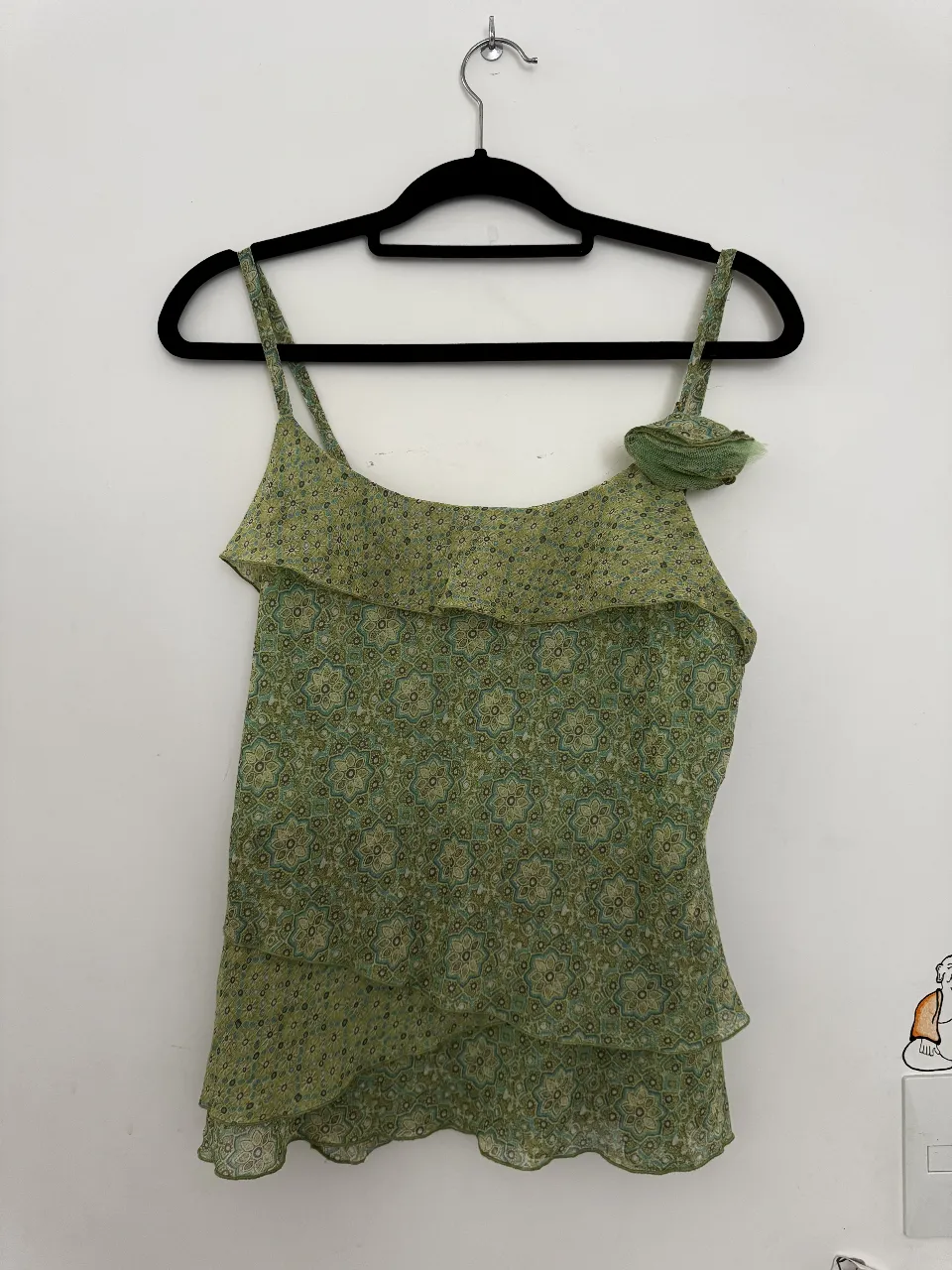 Top verde con estampa floral y volados. Tiene tiras finas y un detalle de flor en el bretel.