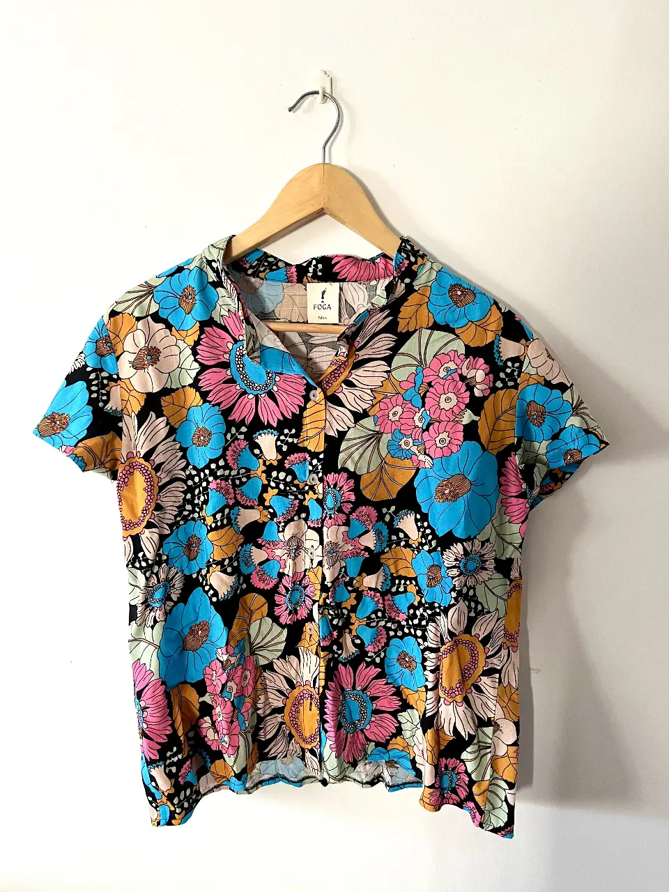 Camisa estampada con flores en tonos vibrantes, ideal para un look retro y llamativo. Confeccionada con un tejido ligero y fresco, perfecta para el verano. Diseño con cuello en V y botones.