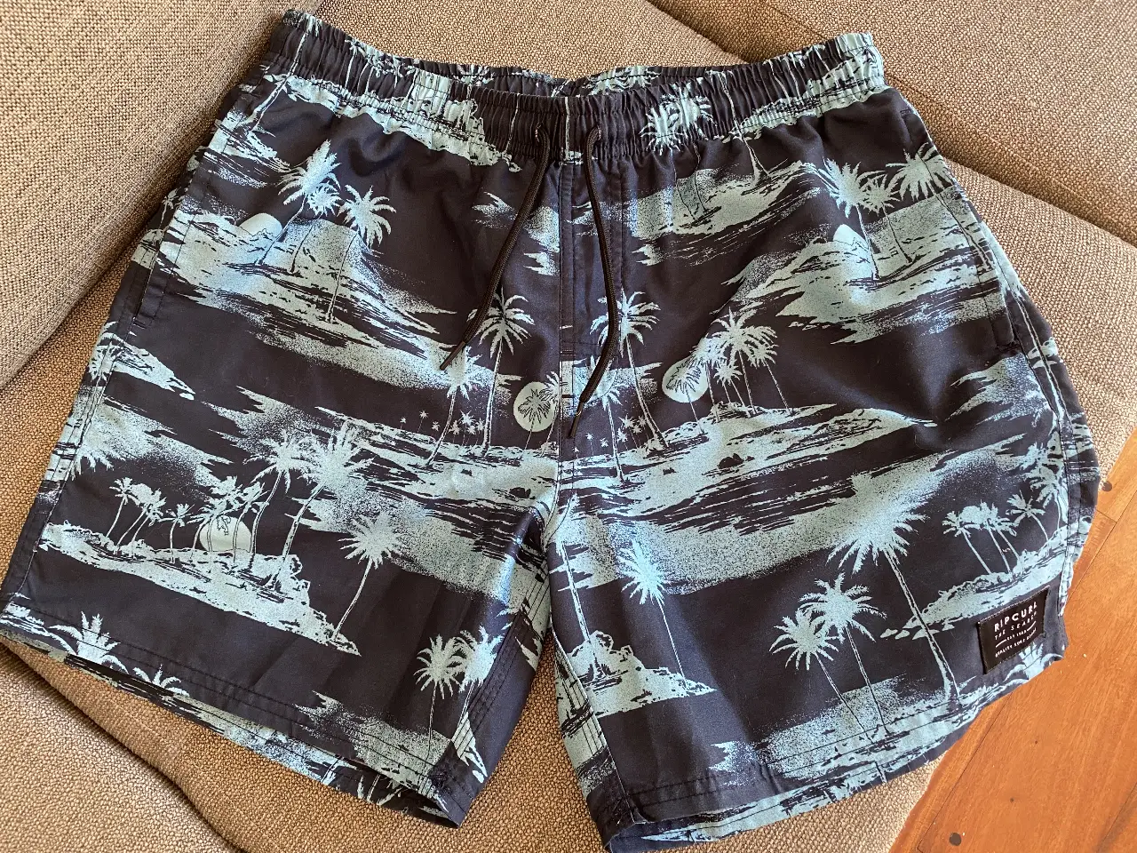 Short de baño Rip Curl para hombre, con estampado de palmeras en tonos azules y negros. Cuenta con cintura elastizada con cordón, bolsillos laterales y uno trasero. Ideal para la playa o pileta. Talle M. 