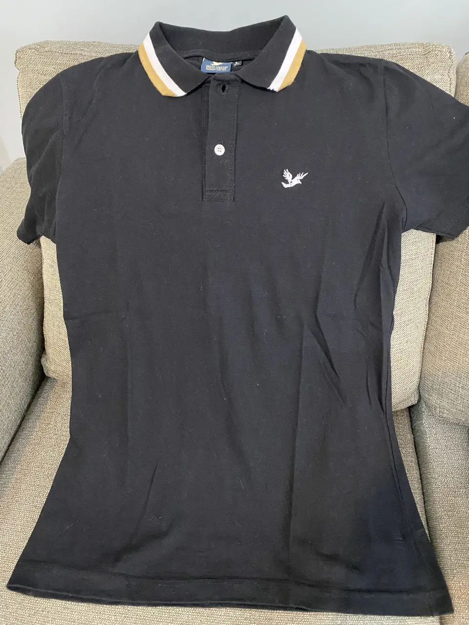 Remera polo negra de hombre, con cuello y detalles en blanco y dorado. Logo de marca bordado en el pecho. Talle S.