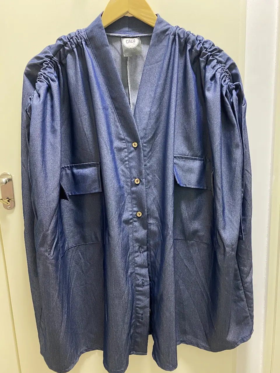 Kimono de jean azul con detalles fruncidos en los hombros. Posee botones dorados y bolsillos delanteros. Ideal para un look casual y moderno. Abarca todos los talles. Nuevo. 