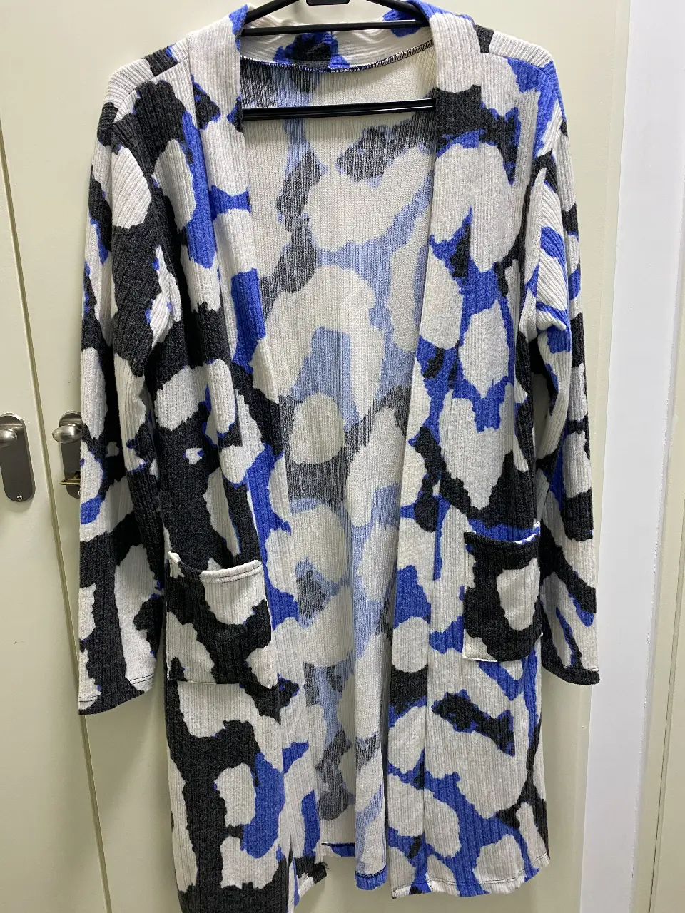 Cardigan largo de lanilla con estampado abstracto en blanco, negro y azul. Posee bolsillos delanteros y un diseño abierto. Ideal para un look casual y moderno.