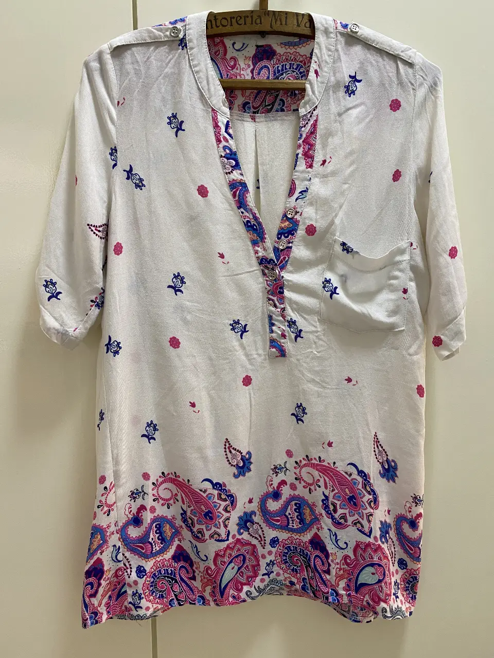 Blusa blanca con estampado floral en tonos rosa y azul. Cuello en V con detalles estampados y mangas 3/4. Un bolsillo en el pecho y botones en la parte delantera. Talle S. 