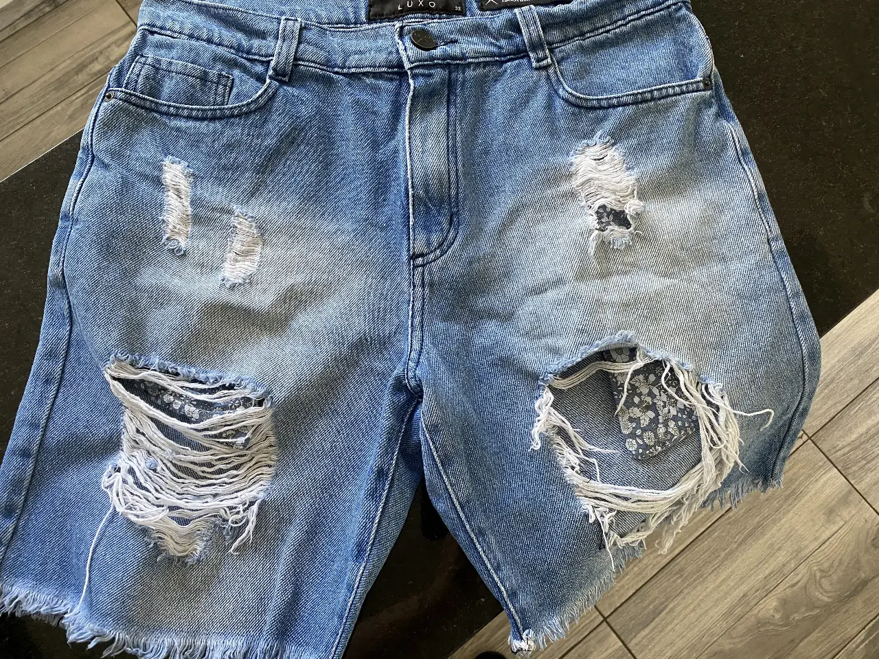 Bermuda marca LUXO de jean azul con roturas y detalles desflecados. Talle 32, ideal para un look casual y moderno.