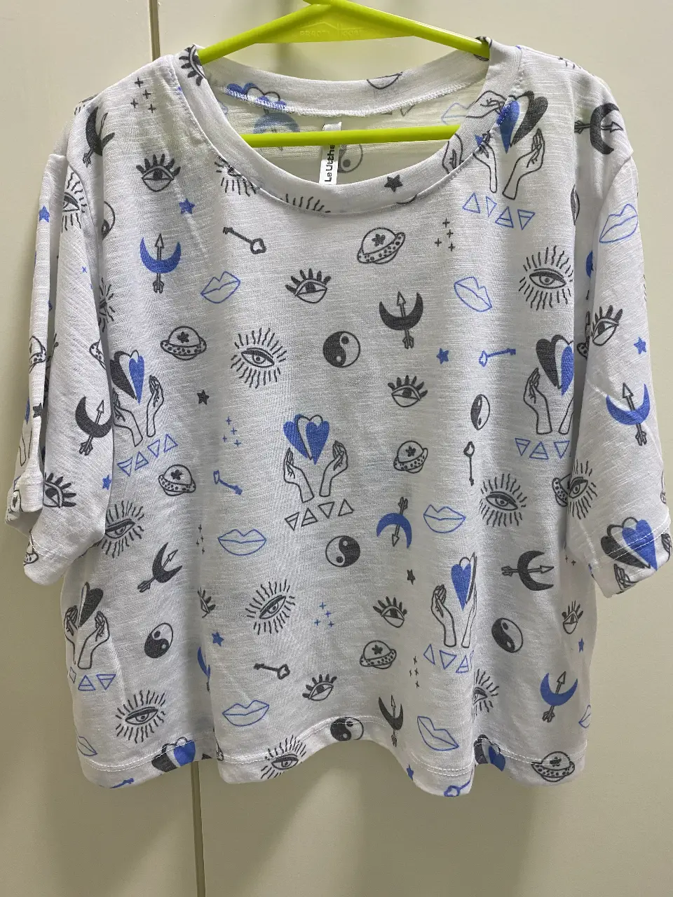 Remera blanca de manga corta con estampado repetitivo de símbolos en azul y negro. Ideal para un look casual y moderno.