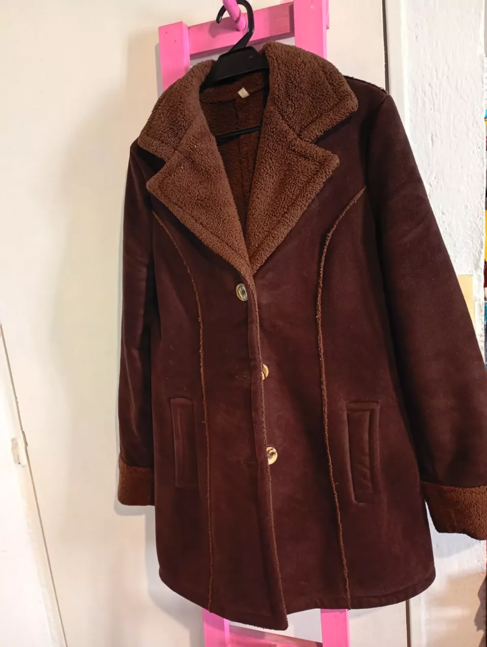 Campera marrón de gamuza sintética con cuello y puños de corderito. Tiene botones dorados y bolsillos frontales.