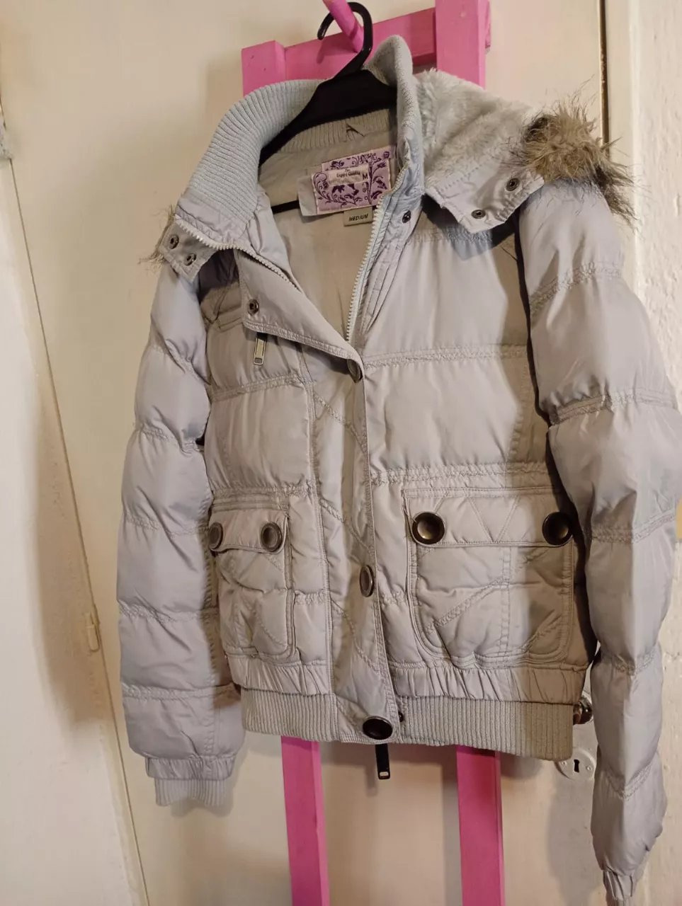 Campera acolchada gris con cuello de piel sintética y capucha. Posee bolsillos frontales con botones y puños y cintura de rib.