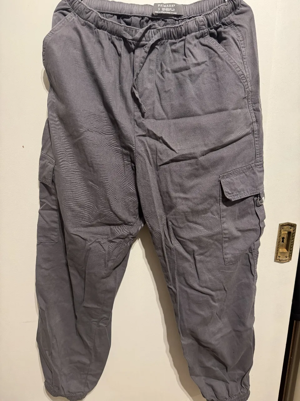 Pantalón cargo gris de hombre, con cintura elastizada y cordón. Bolsillos laterales y en la pierna. Ideal para un look casual y cómodo.