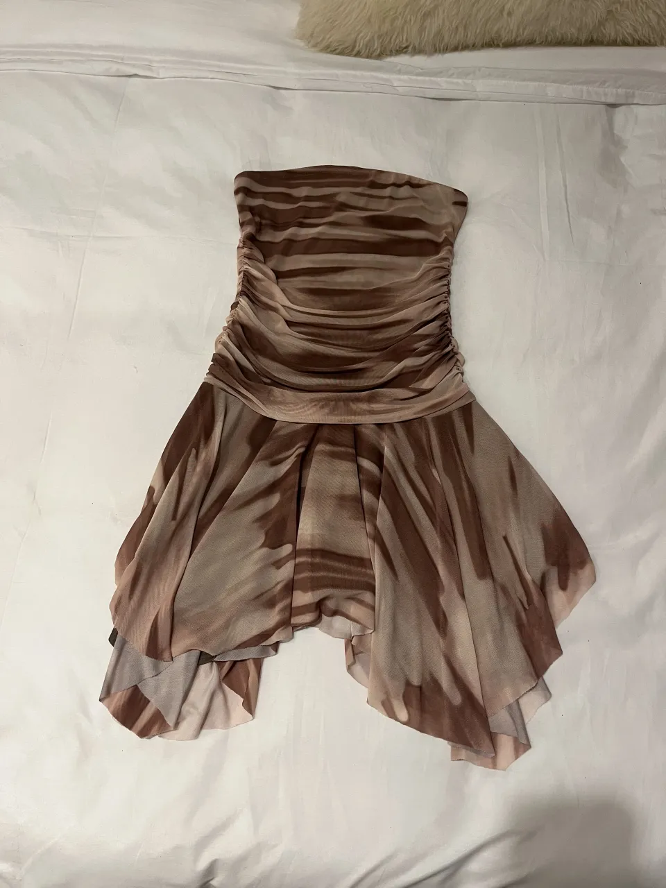 Vestido strapless con fruncido en el torso y estampa abstracta en tonos marrones y beige. La falda tiene un diseño irregular y con movimiento.