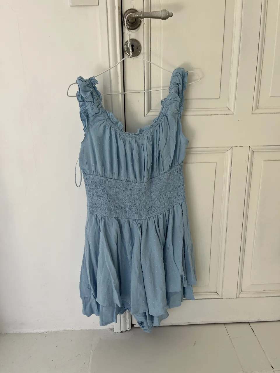 Mono corto celeste con volados en los breteles y detalle de smock en la cintura. Posee pequeños lunares en relieve.