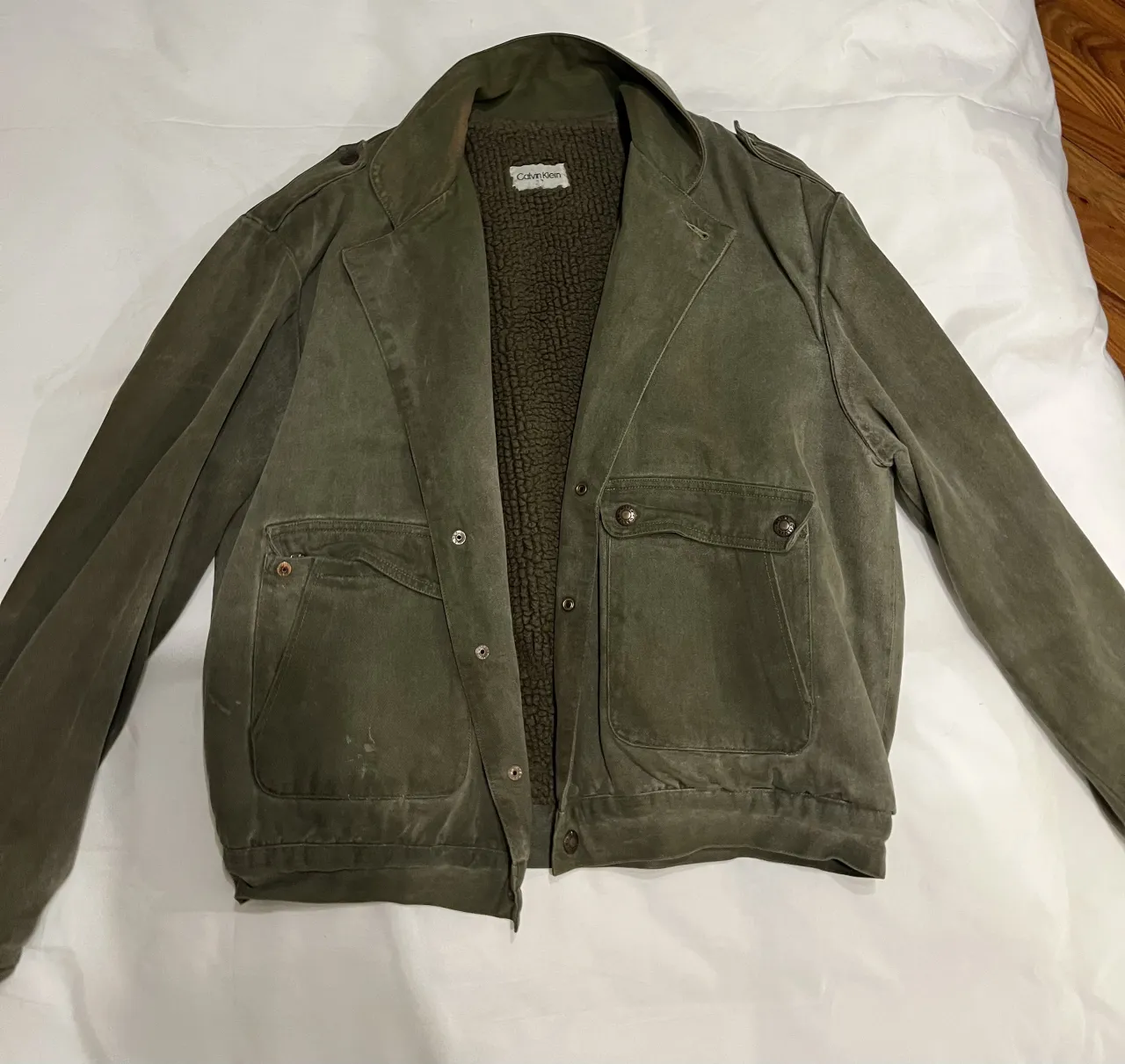 Campera de color verde con cuello, bolsillos frontales y forro interior de peluche.