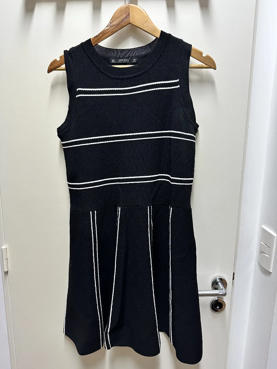 Vestido mini de punto, negro con detalles en blanco. Diseño sin mangas, con franjas horizontales y verticales que estilizan la figura. Ideal para un look moderno y versátil.