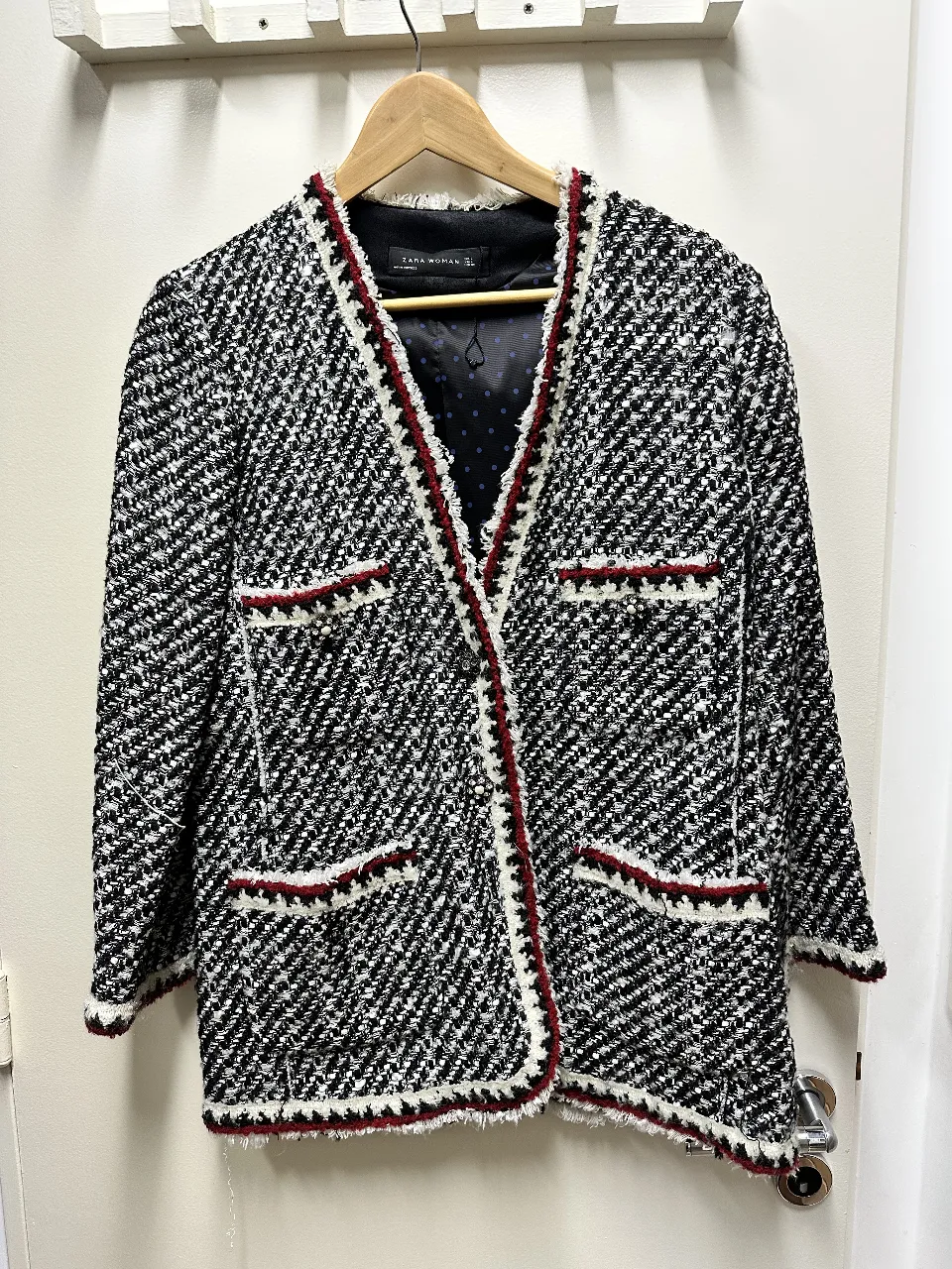 Blazer de tweed en blanco y negro con detalles en rojo. Corte clásico con bolsillos delanteros y forro interior. Ideal para un look elegante y sofisticado.