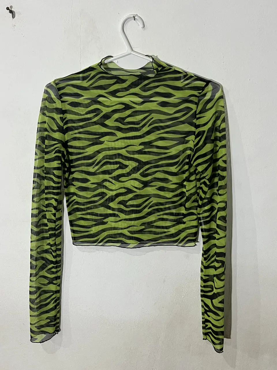 Remera de manga larga con estampado de cebra en verde y negro. Taslúcida. Cuello medio alto y corte crop. Talle S. Ideal para usar con corpiño negro debajo