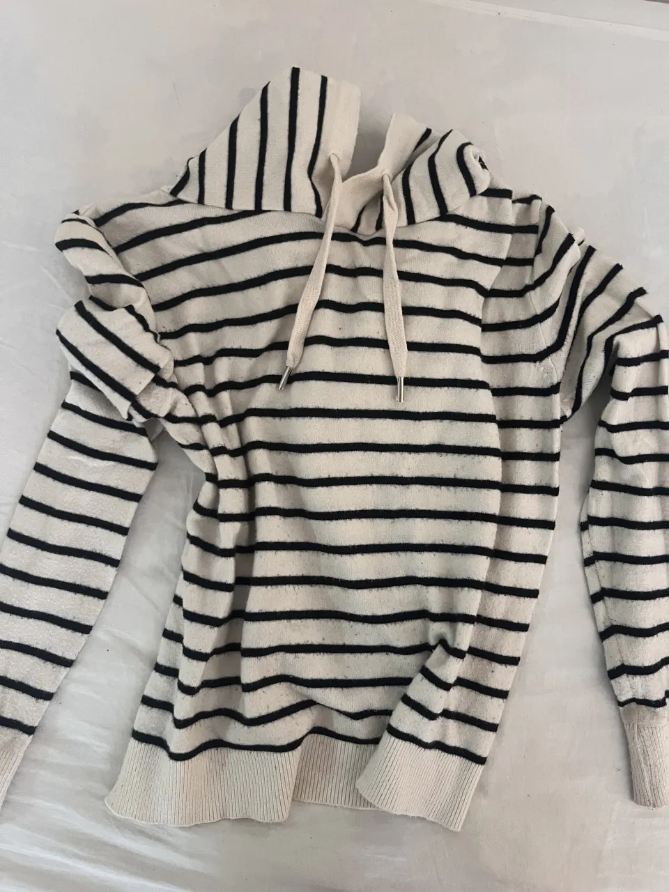 Buzo de franelilla a rayas, con capucha y cordones. Ideal para un look casual y cómodo.