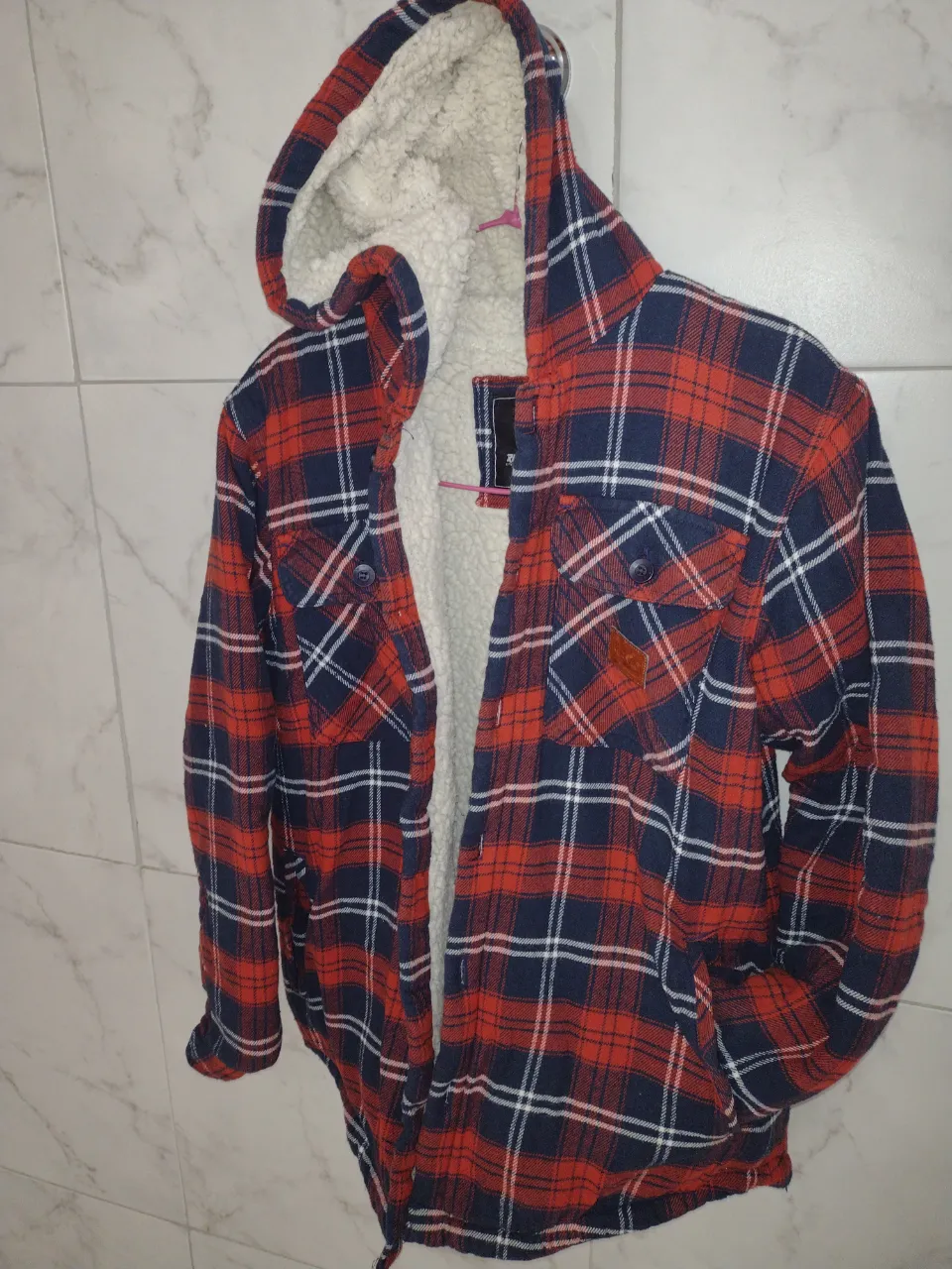 Camisa de leñador con capucha y forro de sherpa, ideal para el invierno. Confeccionada en tela a cuadros rojos y azules, esta camisa ofrece abrigo y estilo. Perfecta para un look casual y abrigado.