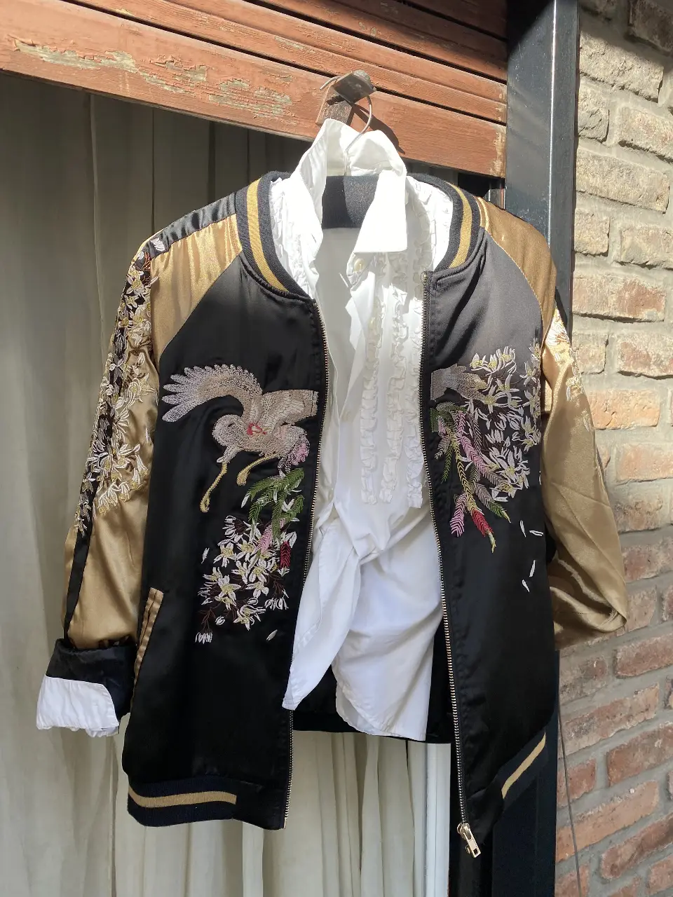 Campera bomber negra con bordados de grullas y flores en dorado y otros colores. Detalles dorados en mangas y cuello. Ideal para un look elegante y con estilo.