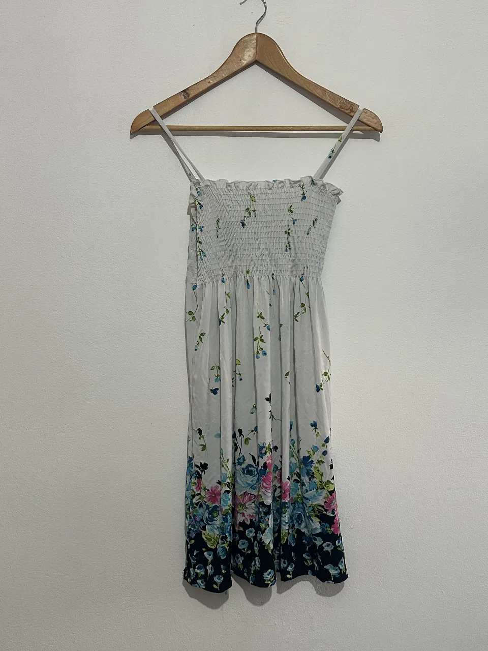 Vestido mini de mujer, con estampado floral en tonos azules y rosas sobre fondo blanco. Tiene tirantes finos y un diseño fruncido en la parte superior, ideal para el verano.