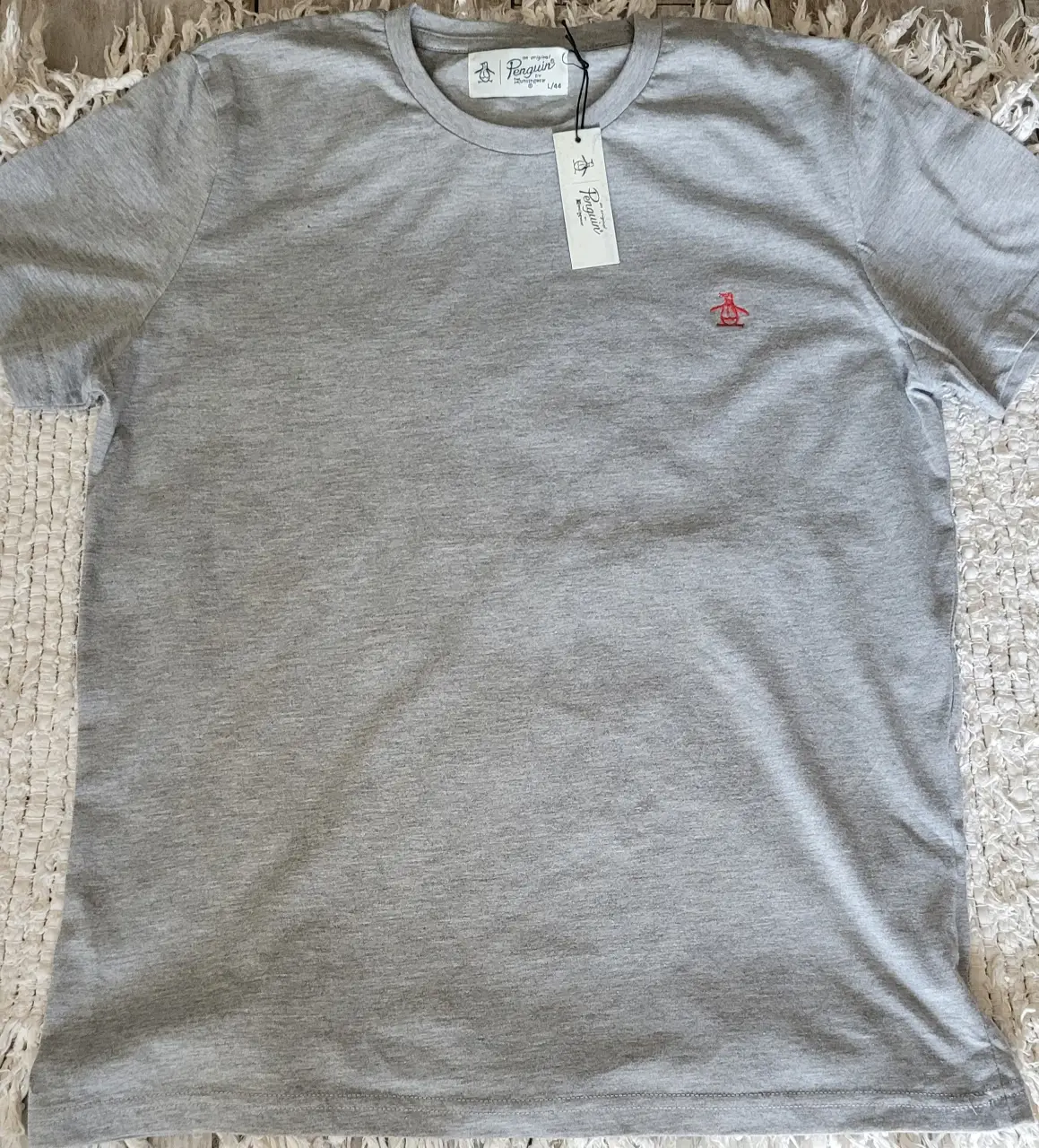 Remera gris de hombre, de la marca Original Penguin, con el logo bordado en rojo. Talle L/44. Tiene una mancha en el pingüino bordado que apenas se nota, se ve en la foto
