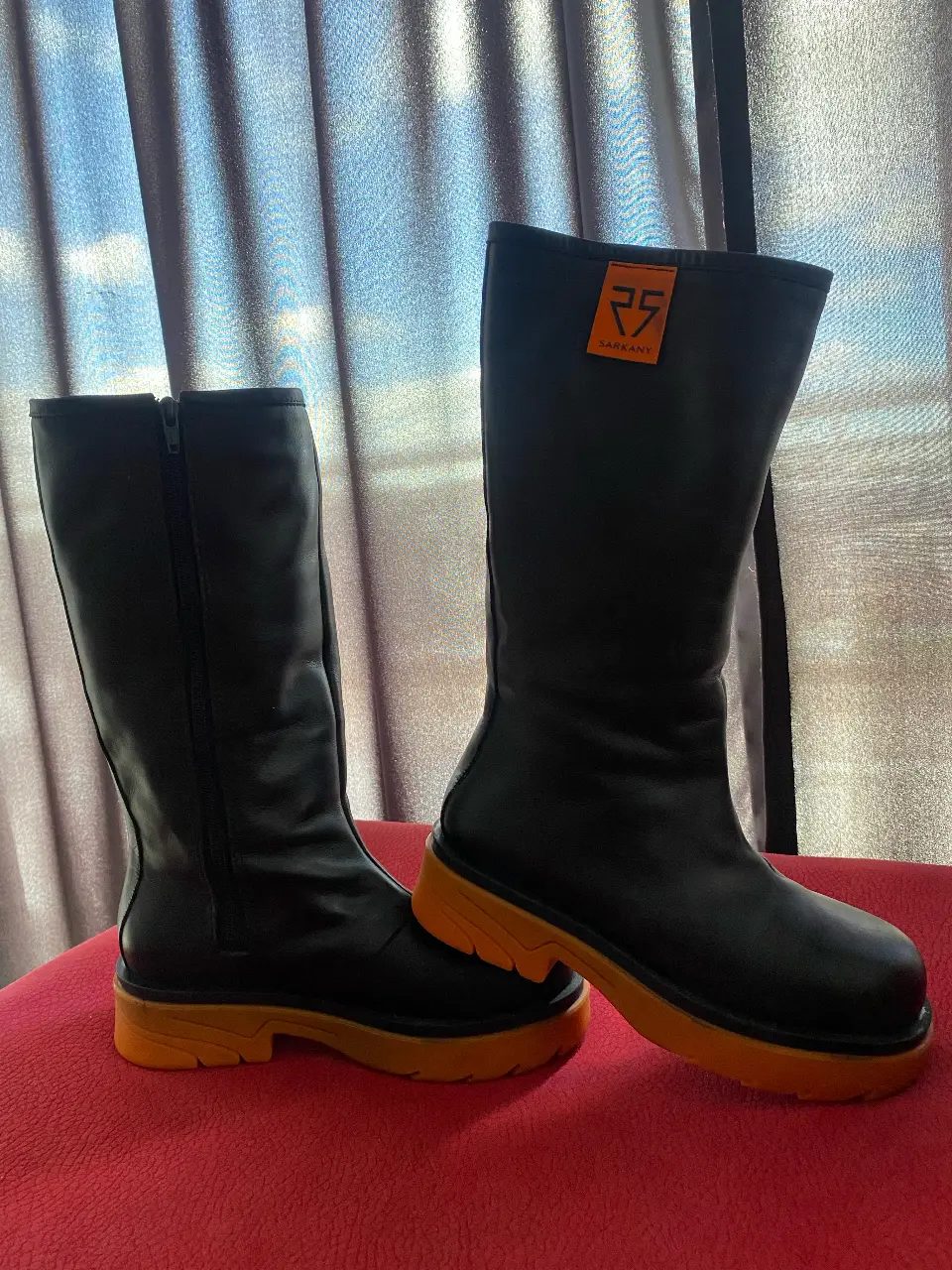 Botas de caña alta negras con suela naranja. Diseño moderno y urbano, ideales para un look audaz y con estilo. Perfectas para destacar en cualquier ocasión.