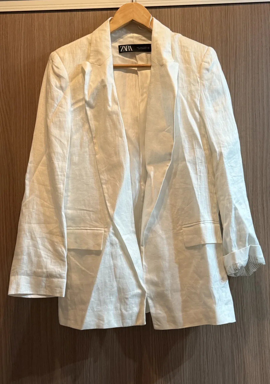 Blazer blanco de lino con solapas clásicas y bolsillos frontales. Mangas largas con puños doblados.