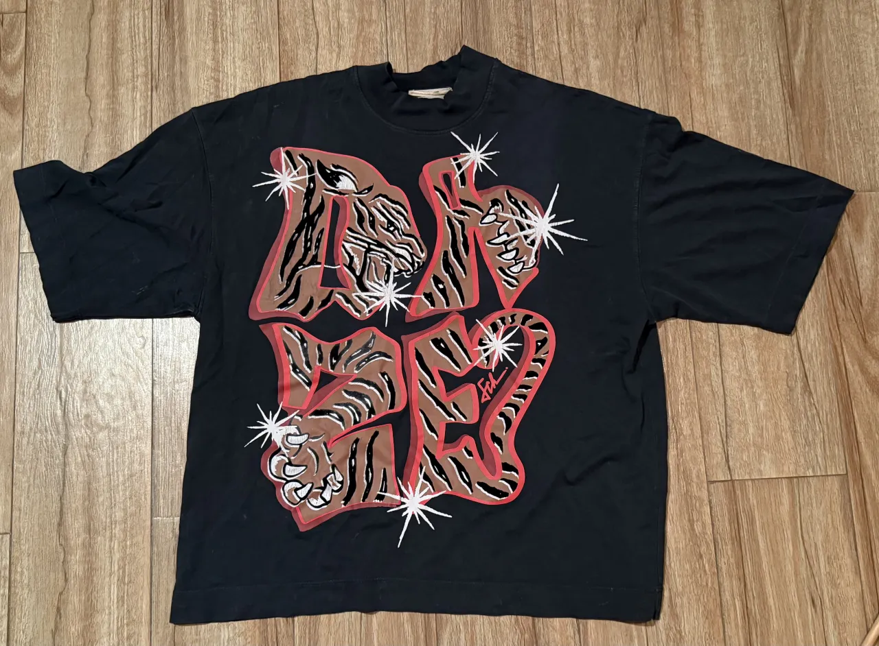 Remera negra con estampa de tigre y letras en color marrón y rojo. La estampa tiene detalles brillantes.