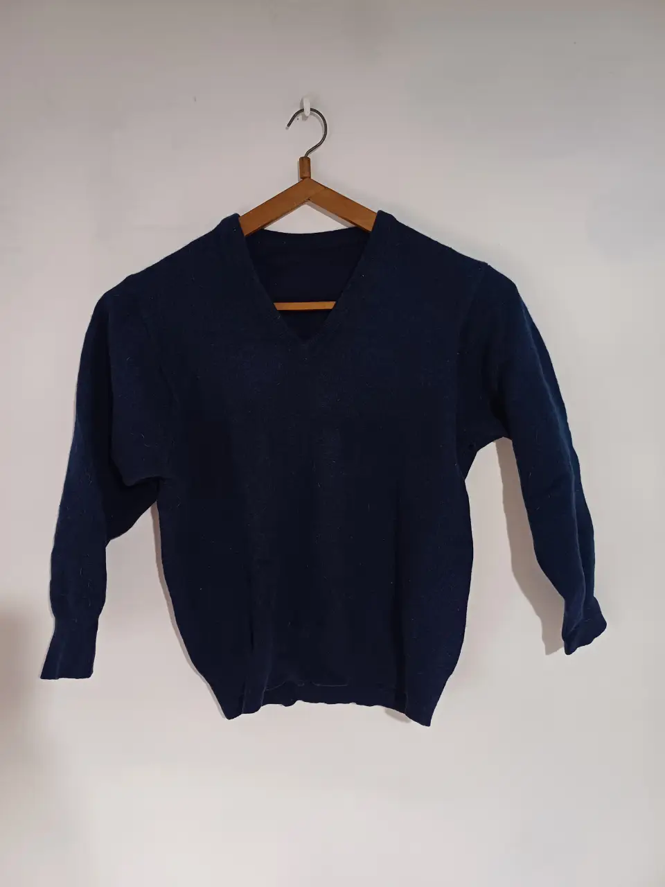 Sweater de lana azul marino con cuello en V. Las mangas quedan cortas.