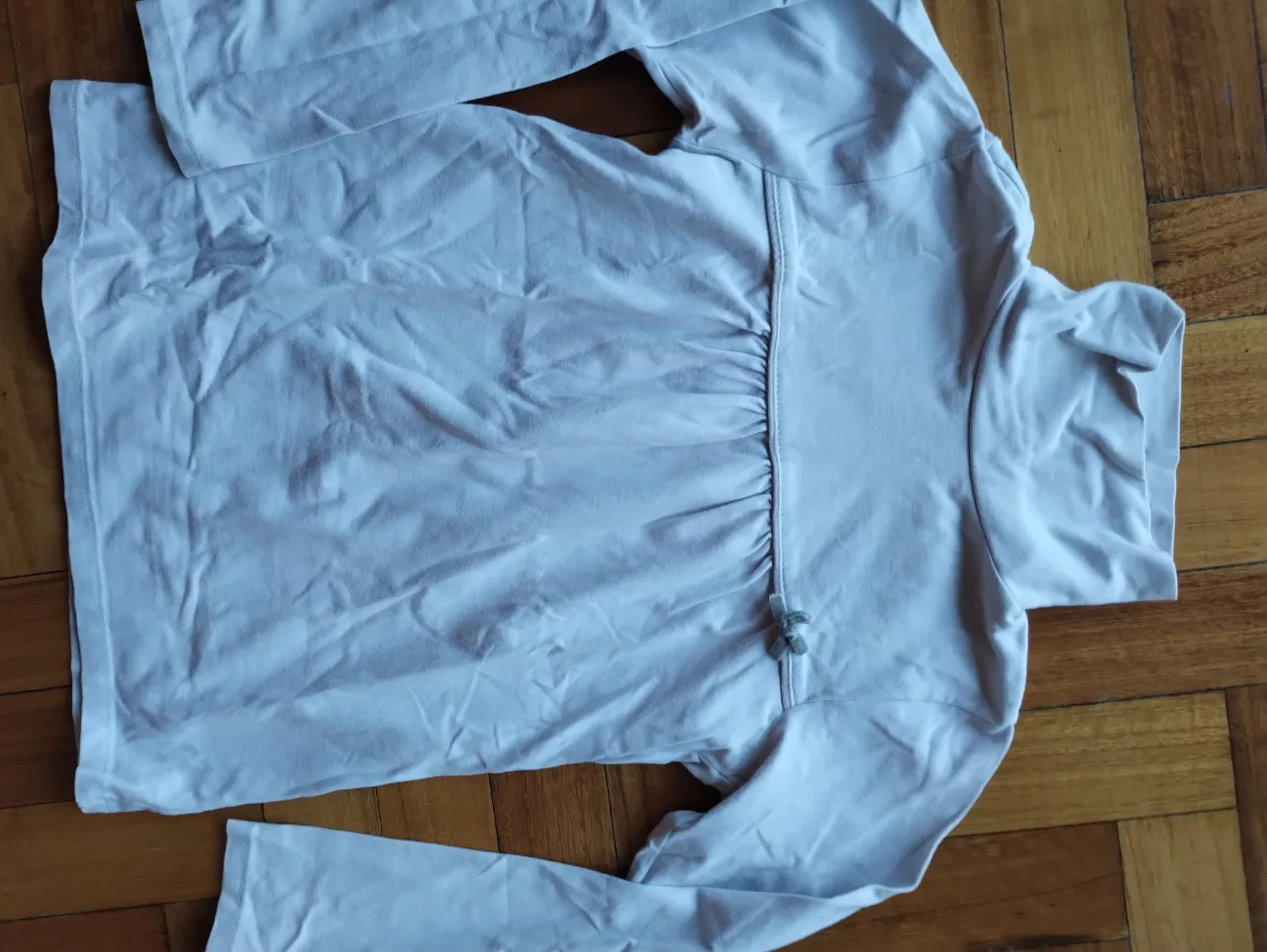 Remera manga larga de color gris clarito, con detalle fruncido en el centro y un pequeño moño. Ideal para un look casual y cómodo.