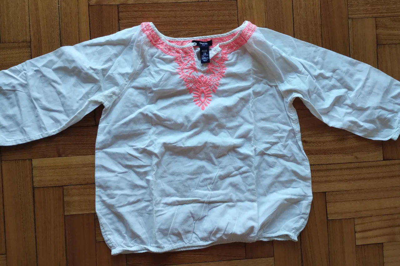 Blusa blanca con detalles bordados en color rosa en el cuello y mangas 3/4. Ideal para un look casual y fresco.