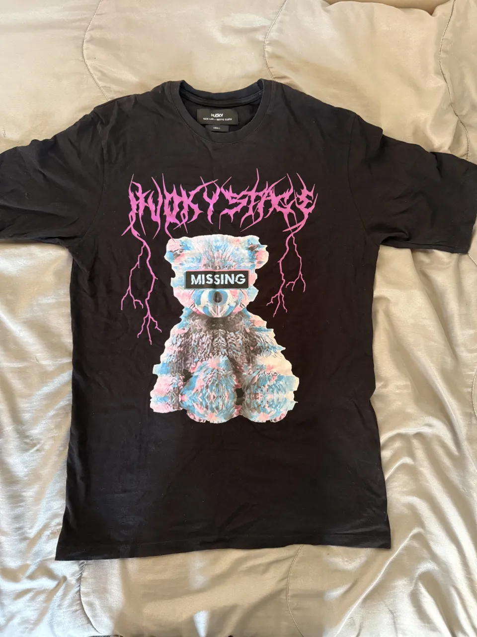 Remera negra con estampa de oso de peluche psicodélico y texto "MISSING". Diseño con estética Y2K y streetwear.