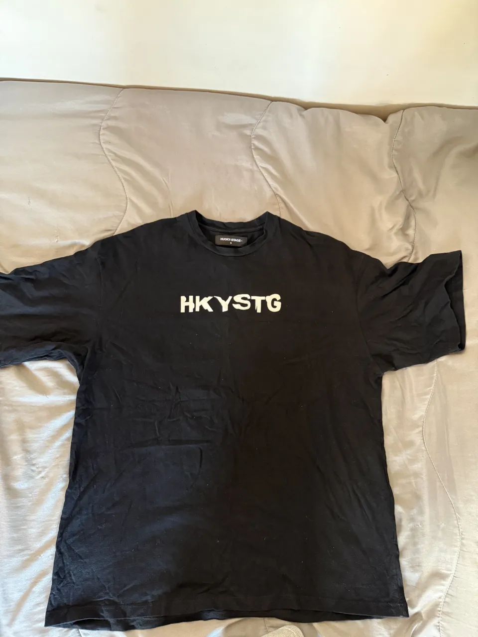 Remera negra oversize con estampa "HKYSTG" en blanco en el frente y un diseño abstracto y colorido en la espalda. Ideal para un look urbano y moderno.