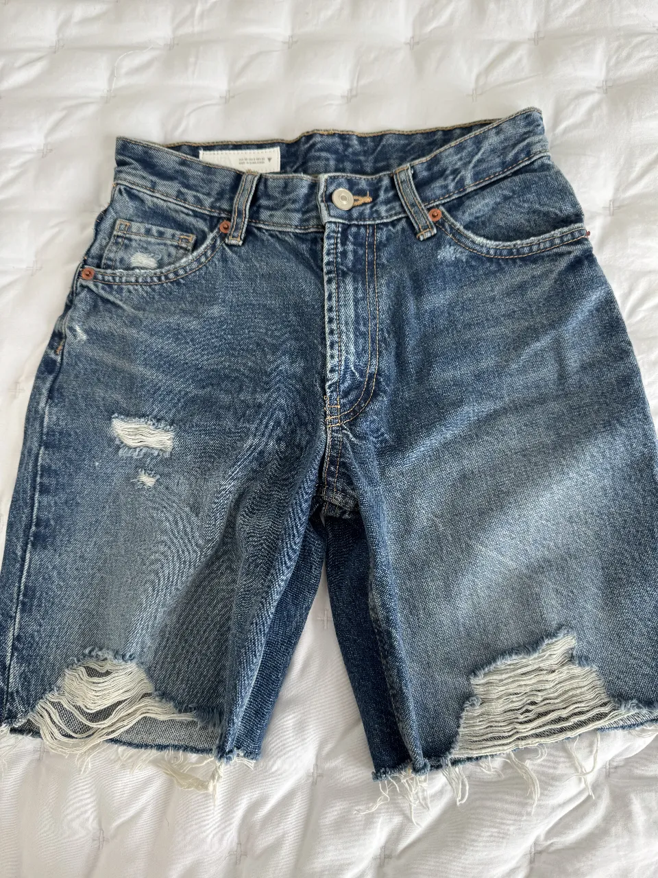 Bermuda de jean azul con roturas y corte desflecado. Talle 32, ideal para un look casual y moderno.