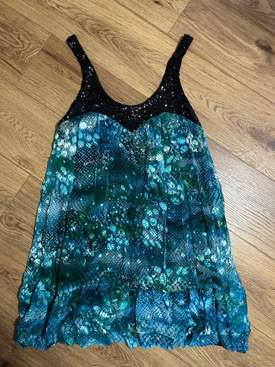 Vestido mini con estampado de serpiente en tonos azules y verdes. Tiene un contorno de corpiño negro con lentejuelas y tirantes. Ideal para una fiesta o salida nocturna.