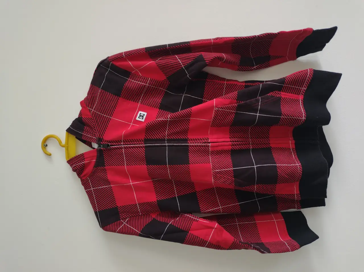 Buzo con cierre para hombre, con diseño a cuadros en rojo y negro. Cuenta con capucha y el logo de la marca DC. Talle M para adolescente. Ideal para un look casual y abrigado.