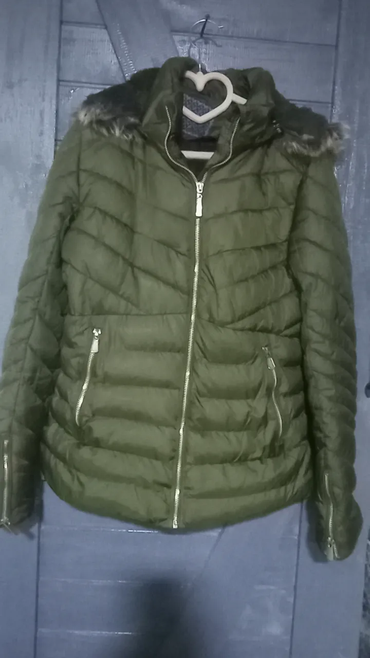 Campera acolchada verde con capucha y detalles de piel sintética en el cuello. Posee cierre central y bolsillos frontales con cierre. Los puños también tienen cierre.