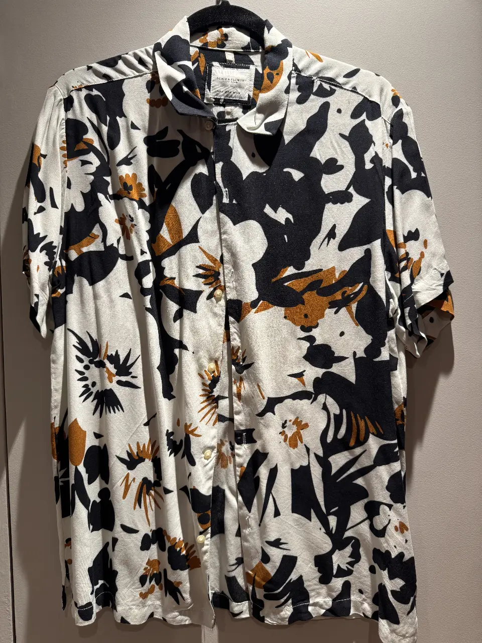 Camisa estampada de hombre, con estampado floral en blanco y negro con detalles en dorado. Cuello clásico y cierre frontal con botones. Ideal para un look casual y moderno.