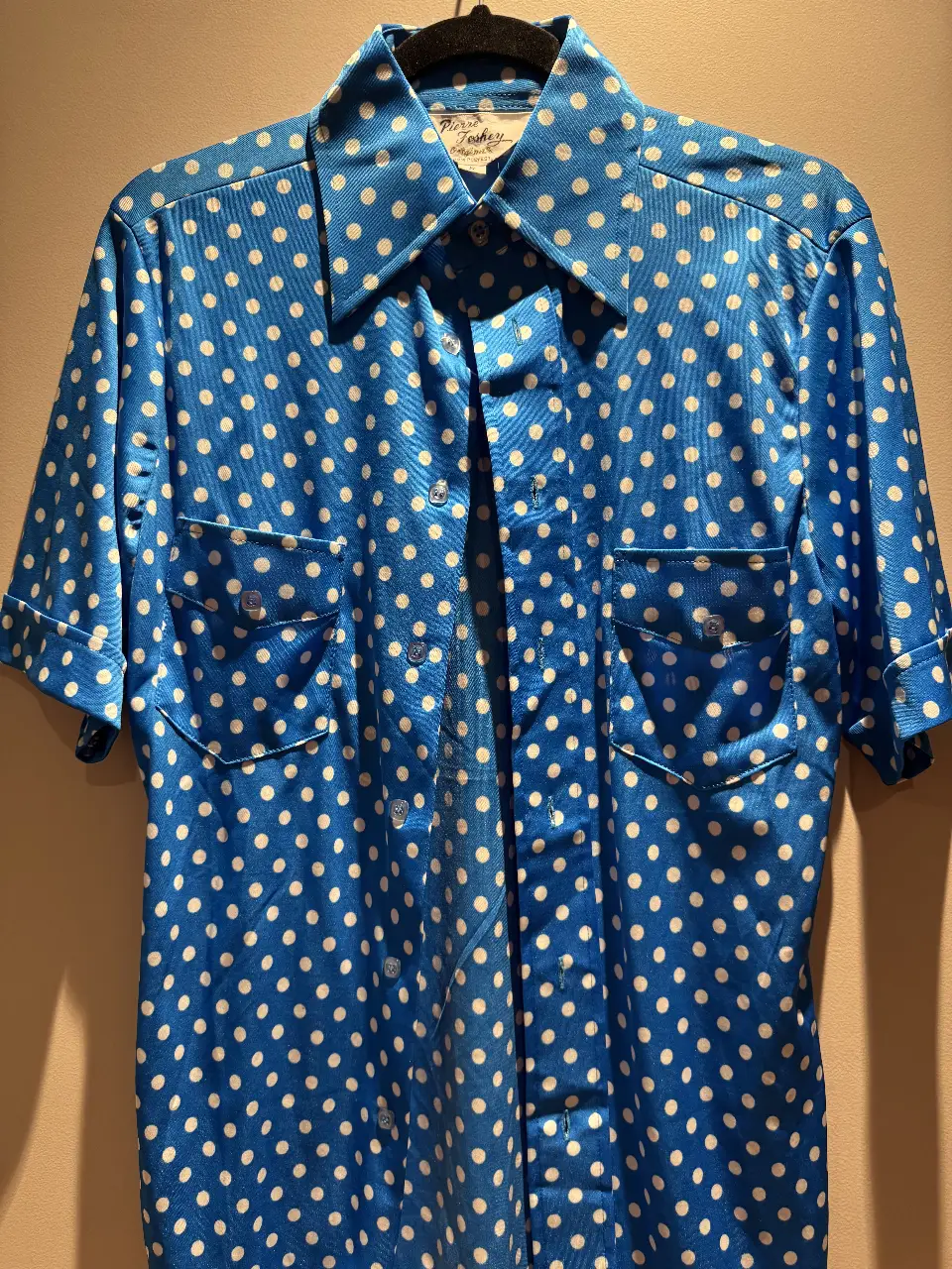 Camisa vintage de hombre con estampado de lunares blancos sobre fondo azul. Corte clásico con dos bolsillos delanteros y mangas cortas. Ideal para un look retro y con onda.