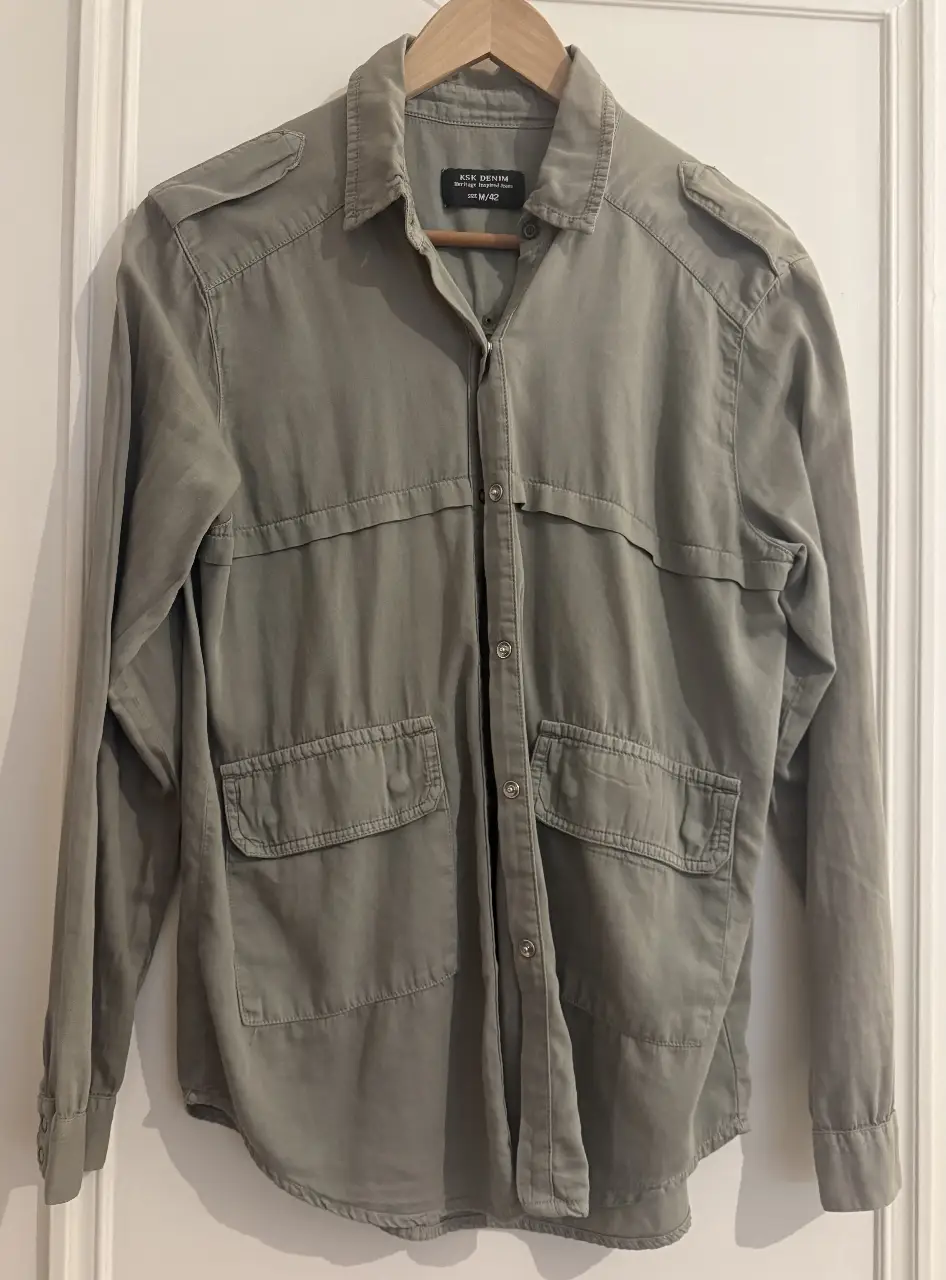 Camisa de hombre estilo militar en color gris con detalles de flecos negros en la espalda. Ideal para un look casual y con onda.