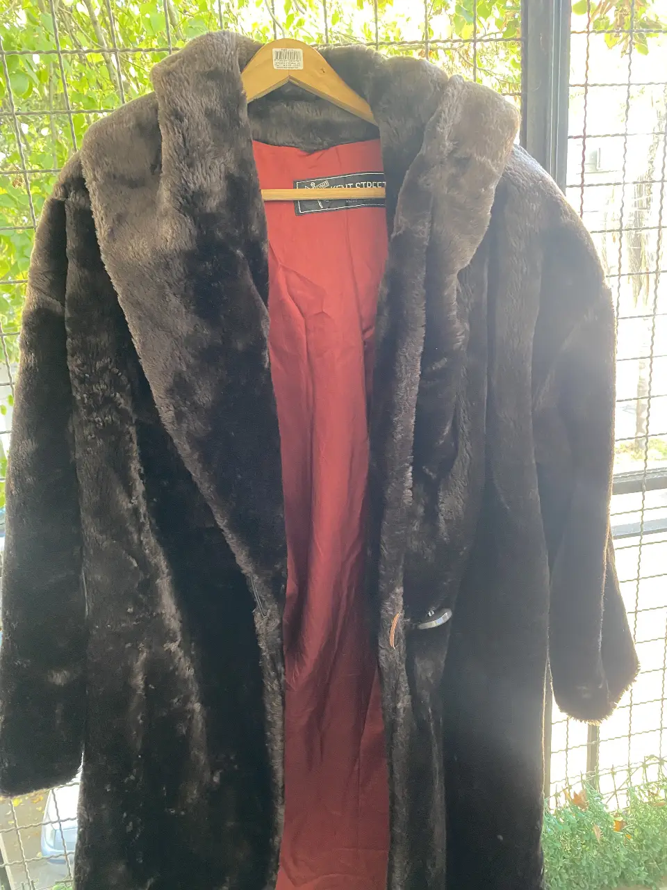 Tapado largo de piel sintética marrón oscuro, con cuello amplio y forro interior rojo. Ideal para un look elegante y abrigado en invierno.