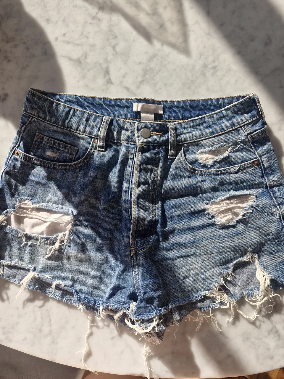Shorts de jean tiro alto con roturas y detalles desflecados. Un clásico para el verano, perfectos para un look casual y canchero. Cintura 39cm, tiro 37cm, cadera 51cm