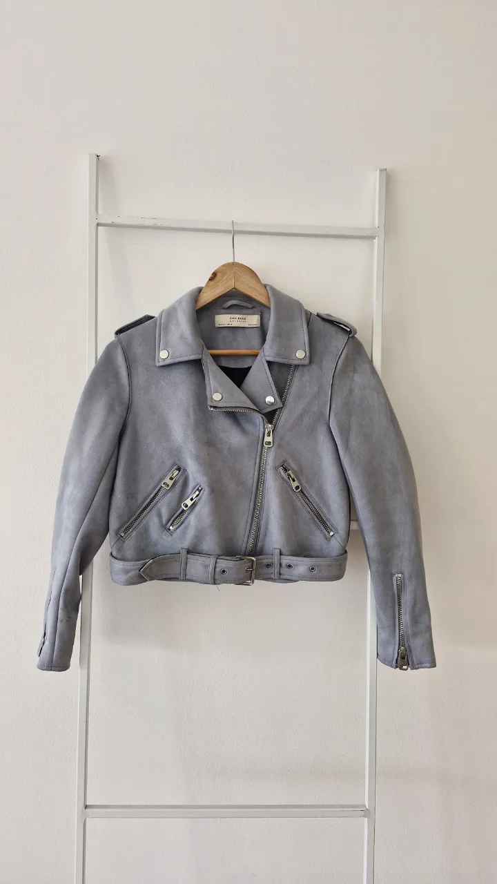 Campera de cuero sintético gris plomo tipo gamuza, estilo biker. Tiene cierre al frente, bolsillos con cierre, cuello solapa y cinturón. Como nueva
