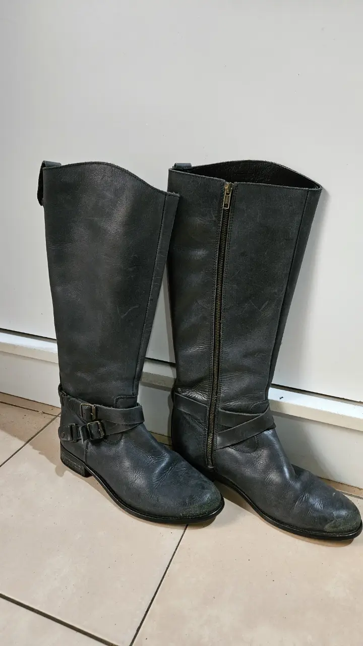 Botas de caña alta de cuero gris oscuro, con cierre lateral y detalles de hebillas. Hechas en España.