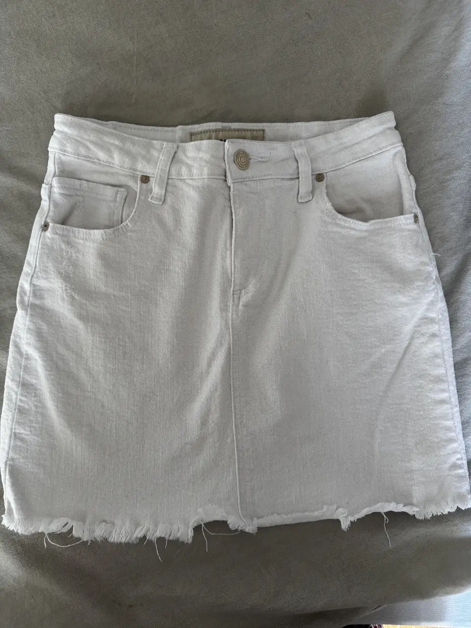 Minifalda de jean blanca de la marca Tucci Jeans, con detalle de flecos en el borde inferior. Talle XS.