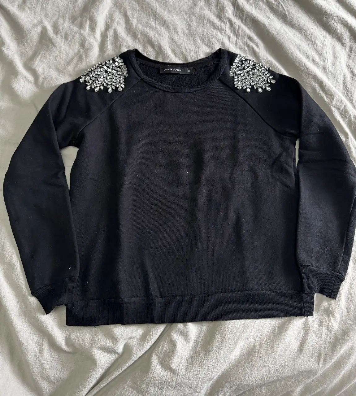 Buzo negro de cuello redondo con apliques de strass en los hombros. Ideal para un look elegante y sofisticado.