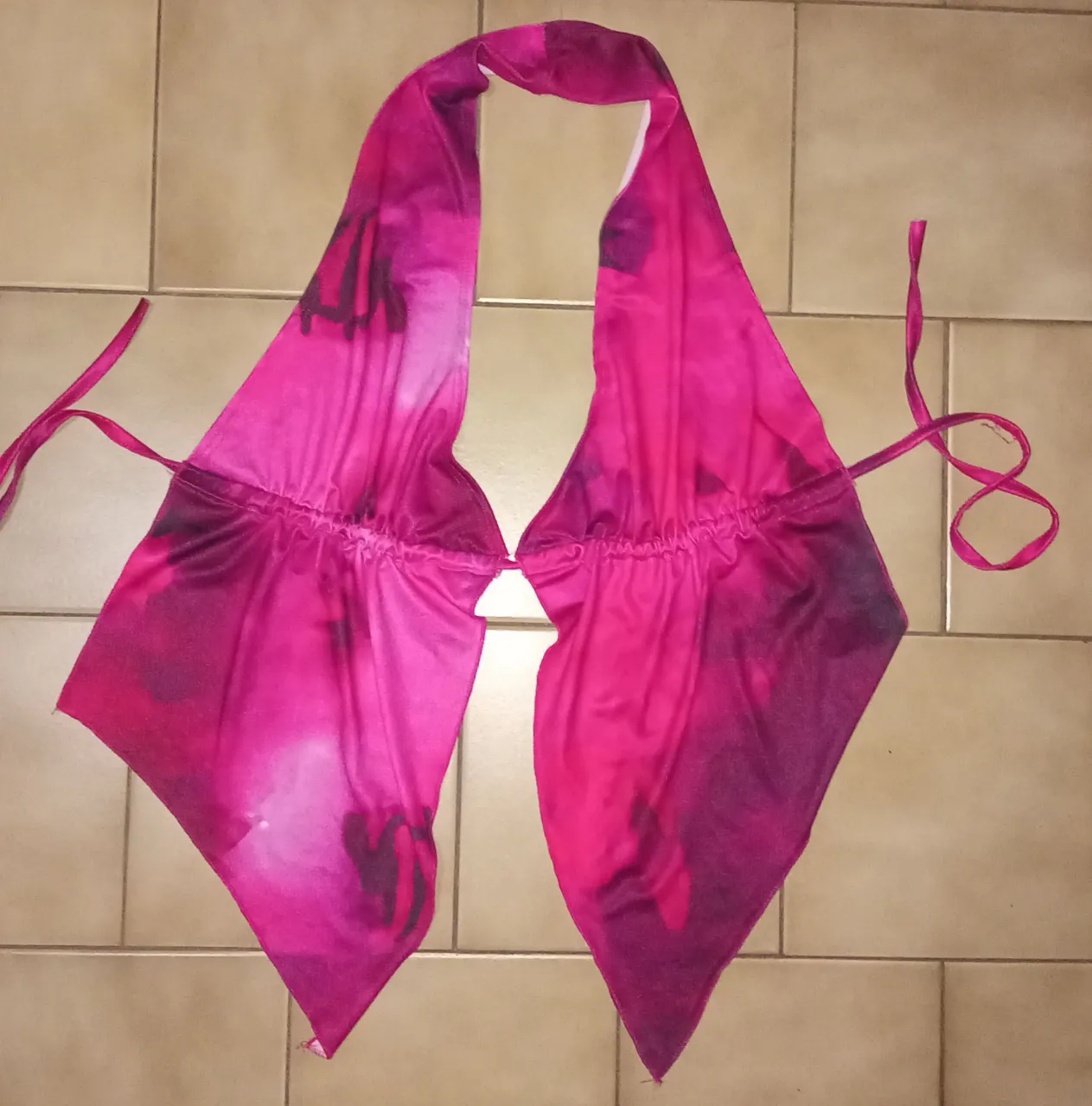 Top de bikini o corpiño estilo halter con estampa vibrante en tonos fucsia y violeta. Posee tiras para atar en cuello y espalda, y detalle de elástico fruncido en el busto para un mejor ajuste. Ideal para lucir en la playa o piscina con mucho estilo.
