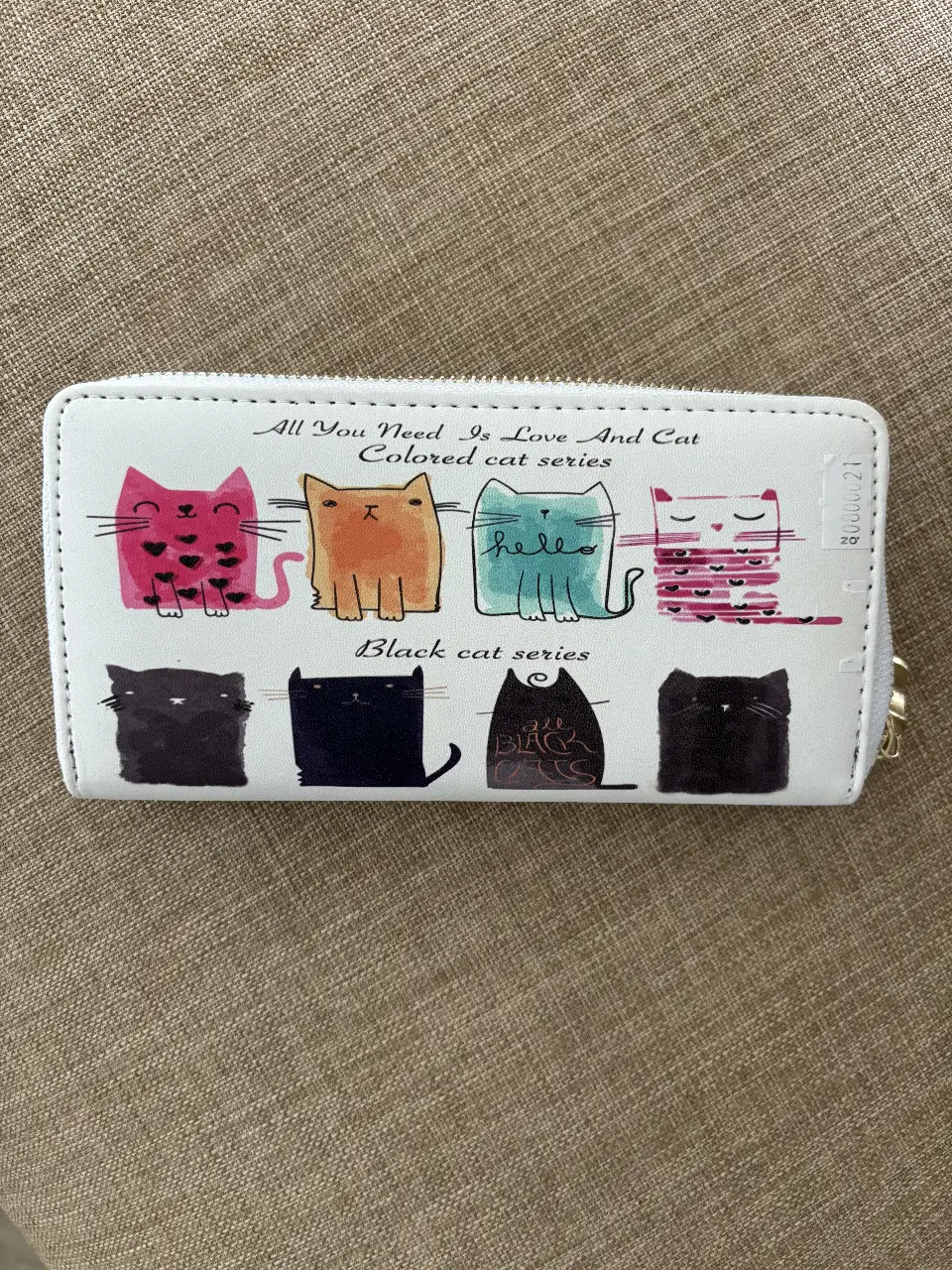 Billetera blanca con diseño de gatos de colores y negros. Cuenta con cierre y múltiples compartimentos internos.